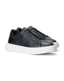 A pair of black leather low-top sneakers with matching black laces and thick white platform soles, shown on a clean white background.