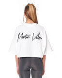 A woman viewed from behind wearing a white cropped T-shirt with 'Martin Valen' printed in black script across the back, paired with dark gray leggings, against a plain white background.