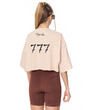 A woman shown from the back wearing a light beige cropped t-shirt with 'Martin Valen' and '777' printed on the back, paired with brown fitted shorts against a white background.