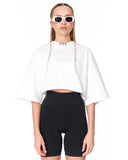 A model wearing a white cropped t-shirt with a high mock neck and wide short sleeves, paired with black bike shorts and white-framed sunglasses. The shirt features the number '777' printed in black near the collar.