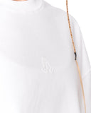 Close-up of a white crewneck sweatshirt featuring a tonal embroidered praying hands logo on the left chest, with a braided tan strap running vertically along the right side.