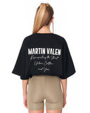 A woman shown from the back wearing a black Martin Valen graphic t-shirt and beige fitted shorts against a plain white background.