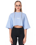 A model wearing a light blue cropped t-shirt with 'MARTIN VALEN' printed in white on the chest, paired with black leggings, against a plain white background.