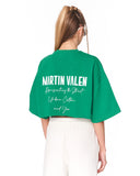 A model shown from the back wearing a bright green cropped T-shirt with 'MARTIN VALEN' printed in white across the back, paired with white pants, against a plain white background.