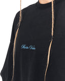 A close-up of a person wearing an oversized black t-shirt with 'Martin Jarler' embroidered in light blue cursive on the chest. The person has blonde braided hair hanging down the front of the shirt against a plain white background.