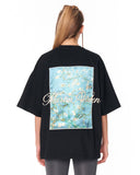 A woman shown from the back wearing an oversized black t-shirt with a large graphic print of Van Gogh's 'Almond Blossom' in light blue, white, and green, with 'Martin Valen' written in white script across the center.