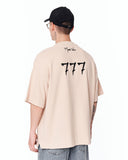 ‘777’ Men’s Oversized Beige Designer T-shirt with 3D Print Detail worn with a black cap and round sunglasses
