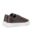 A pair of dark brown leather low-top sneakers with white platform soles, shown from a three-quarters angle on a white background.
