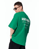 "Slogan" Men’s Oversized Printed Designer T-shirt in Green worn with dark sunglasses and white low-top sneakers