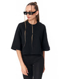 A woman modeling a black cropped t-shirt with three-quarter sleeves and black pants against a plain white background.