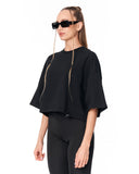 A woman modeling a black cropped short-sleeve top with wide draped sleeves and matching black leggings against a plain white background.