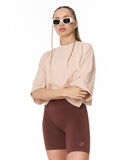 A woman modeling a light beige short-sleeve top and dark brown fitted biker shorts against a plain white background.