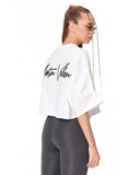 A woman shown from the back wearing a white cropped t-shirt with a black script logo reading 'Martin Valen' and dark gray leggings, photographed against a solid white background.