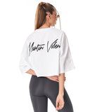 A woman shown from the back wearing a white cropped T-shirt with a black 'Martin Walker' script logo on the back, paired with dark gray capri leggings and white sneakers, against a plain white studio background.