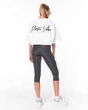 A woman shown from the back wearing a white cropped T-shirt with a black 'Martin Walker' script logo on the back, paired with dark gray capri leggings and white sneakers, against a plain white studio background.