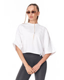 A woman modeling a white cropped tunic top with wide, draped sleeves and a front zipper, paired with dark gray leggings, against a plain white background.
