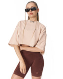 A model wearing a light beige cropped short-sleeve top and dark brown fitted biker shorts, styled with black chain-link sunglasses against a plain white background.