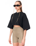 A model wearing a black short-sleeve crop top with wide bell sleeves and beige high-waisted bike shorts, styled with black sunglasses and a gold chain necklace against a plain white background.