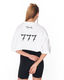 A woman shown from the back wearing a white oversized crop top with 'Martin Valen' and the number '777' printed in black on the back, paired with black bike shorts against a white background.