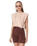 A model wearing a light beige sleeveless crop top and dark brown fitted biker shorts against a plain white background.