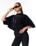 A woman modeling a black cropped top with wide short sleeves, a high mock neck, and a gold front zipper. The top features a small white script logo on the left chest.