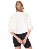 A woman shown from the back wearing a white cropped short-sleeve top and black biker shorts against a plain white background.