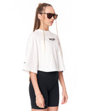 A model wearing a white cropped t-shirt with a black 'Martin Valen' logo on the chest, paired with black bike shorts and sunglasses with chain straps, against a plain white background.