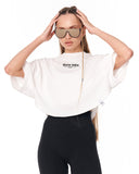 A model wearing a white cropped t-shirt with 'Martin Valen' printed on the chest, paired with black leggings and sunglasses, against a plain white background.