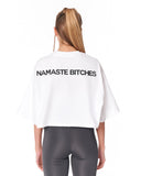 A woman viewed from the back wearing a white cropped T-shirt with the text 'NAMASTE' printed in black across the upper back, paired with dark gray leggings, against a plain white background.