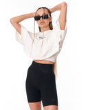 A woman modeling a white cropped t-shirt and black biker shorts against a plain white background.