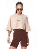 A model wearing a cropped beige t-shirt with 'MARTIN VALEN' printed on the chest and dark brown fitted biker shorts, set against a plain white background.