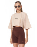 A model wearing a beige cropped t-shirt with 'MARTIN VALEN' printed on the chest and dark brown high-waisted biker shorts, set against a plain white background.