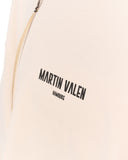 Close-up of a light beige or cream-colored garment with black printed text reading 'MARTIN VALEN' and a small portion of a zipper visible at the top left.