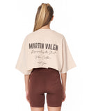 A woman shown from the back wearing a light beige Martin Valen crop top and brown bike shorts against a plain white background.