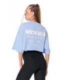 A woman shown from the back wearing a light blue cropped T-shirt with white 'MARTIN VALEN' text and black leggings against a plain white background.
