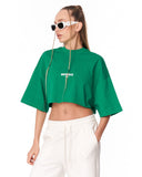 A model wearing a bright green cropped t-shirt with a white 'MARTIN VALEN' logo on the chest, paired with white drawstring pants and white-framed sunglasses, against a plain white background.
