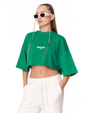 A model wearing a bright green cropped t-shirt with a white 'MARTIN VALEN' logo on the chest, paired with white sweatpants and white-framed sunglasses, against a plain white background.