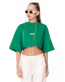 A model wearing a bright green cropped t-shirt with a white 'MARTIN VALEN' logo on the chest, paired with white sweatpants and white-framed sunglasses, against a plain white background.