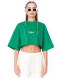 A model wearing a bright green cropped t-shirt with 'MARTIN VALEN' printed in white on the chest, paired with white sweatpants and white-framed sunglasses, against a plain white background.