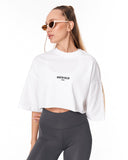 A woman wearing a white cropped t-shirt with 'MARTIN VALEN' printed in black on the chest, paired with dark gray leggings, set against a plain white background.
