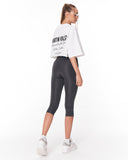 A woman shown from the back wearing a white cropped t-shirt with black text and dark gray capri leggings, paired with white sneakers, against a plain white background.